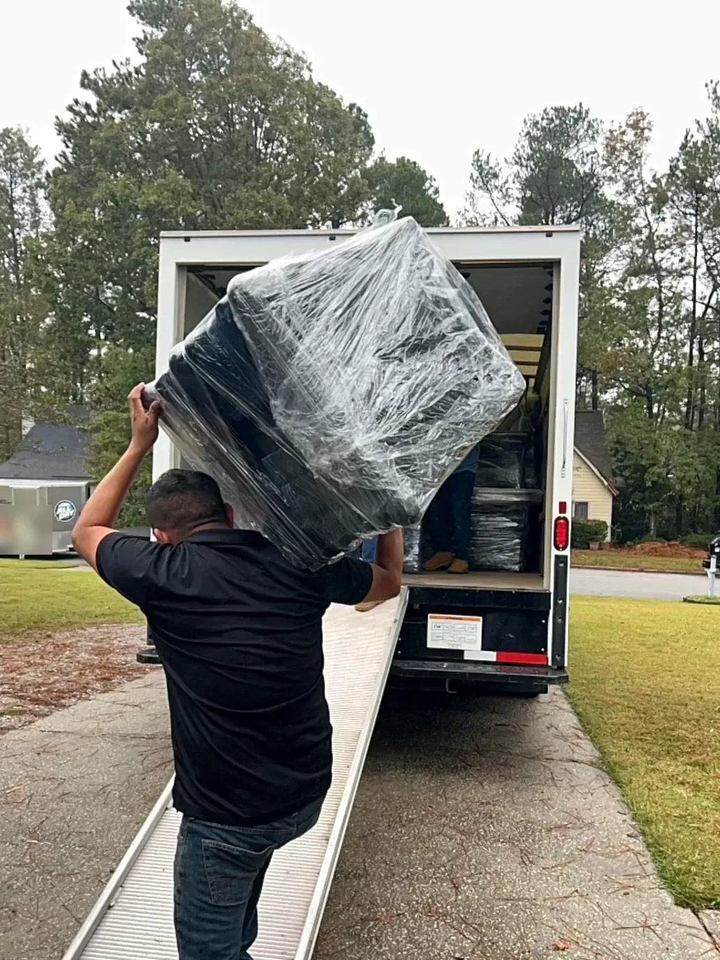 Technician carrying shrink-wrapped furniture into a moving truck during pack-out